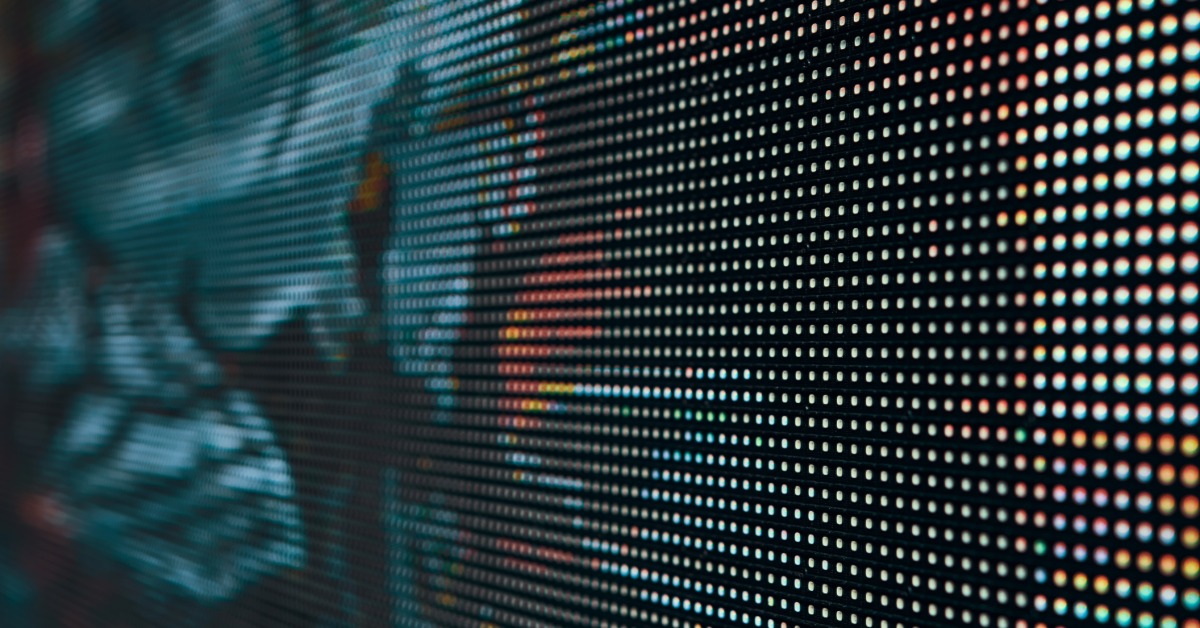 A blurred LED screen showing bright blue, green, and red lights in an abstract digital pattern across the screen surface.