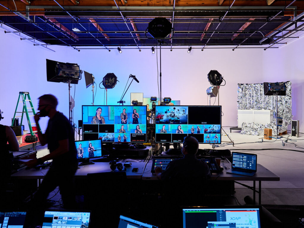 Live stream production control station with multiple monitors and lighting on a corporate event set.